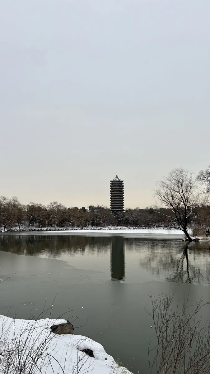 The Boya Pagoda reflected in the partly frozen Weiming Lake at Peking University in Beijing, snow along the banks under a pale winter sky.