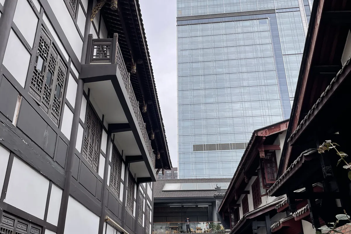 Traditional black-timber-and-white lanes of Chengdu's Taikoo Li, beside the ancient Daci Temple, framing a modern glass skyscraper rising behind — the city's ancient-and-modern blend in a single view.
