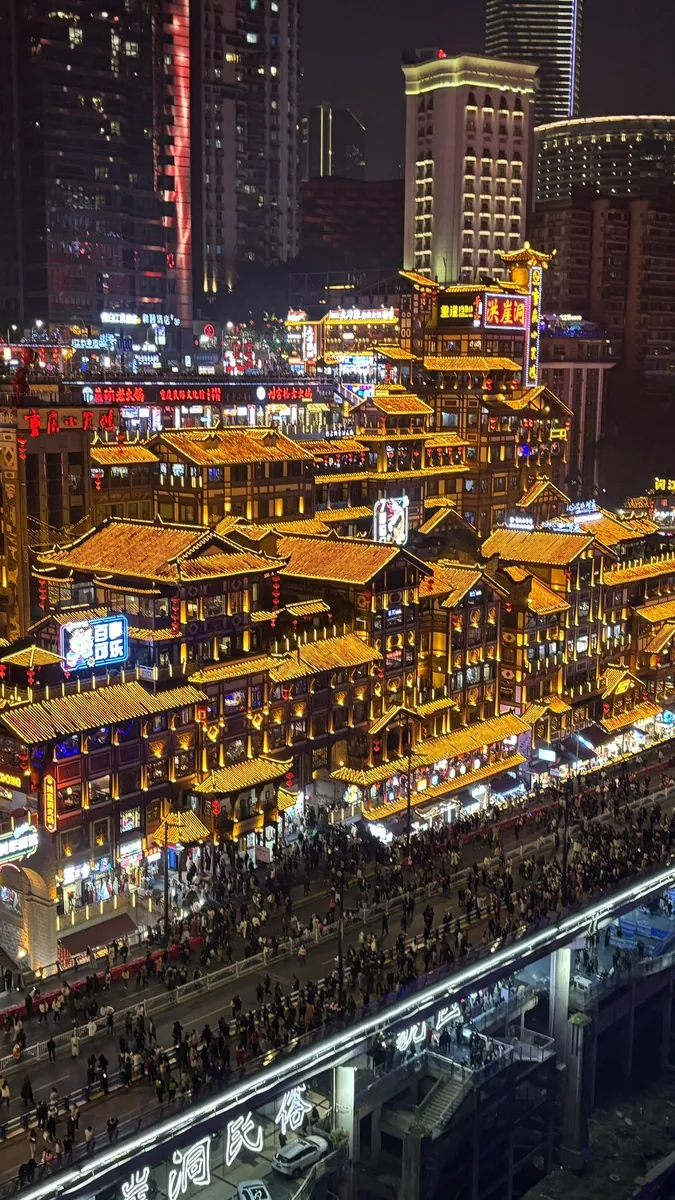 The Hongya Cave stilt-house complex in Chongqing lit gold at night, its tiered traditional rooftops stacked up the riverbank below modern towers.