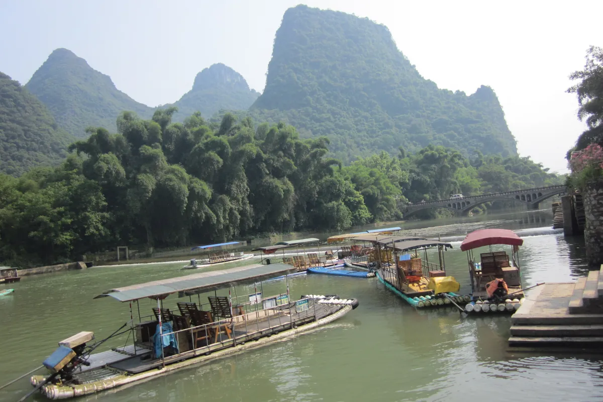 Karst peaks rising over bamboo groves, with traditional rafts moored on the Li River near Yangshuo, Guilin.