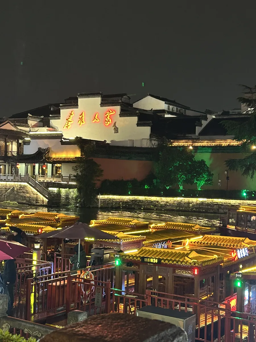 The Confucius Temple (Fuzimiao) and Qinhuai riverside in Nanjing lit up warmly at night, the traditional roofs and lanterns mirrored in the water.