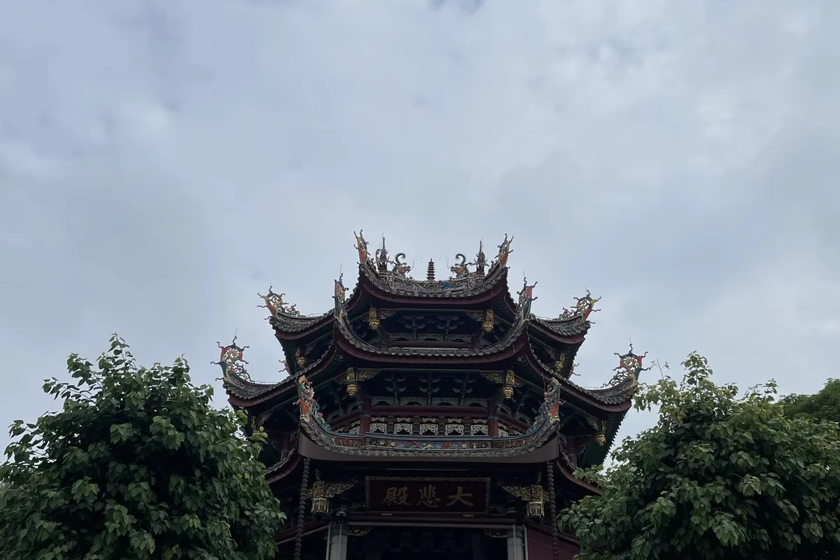 The ornate, tiered rooftop of Nanputuo Temple's Great Compassion Hall in Xiamen, framed by trees against a cloudy sky.